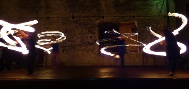 Mehrere Feuerspieler der Gruppe Claymore auf der Bühne vor der feuerfesten Rückwand, mit wirbelnden Feuertrails.