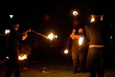 Feuerspieler in mittelalterlicher Gewandung mit brennenden Flammenstäben vor Publikum.